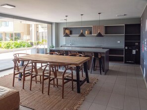 A modern kitchen with a dining area, featuring a wooden table and chairs, pendant lighting, and a view of the outdoors. - Costa Home - 2P Vistas Mauco (Concón)