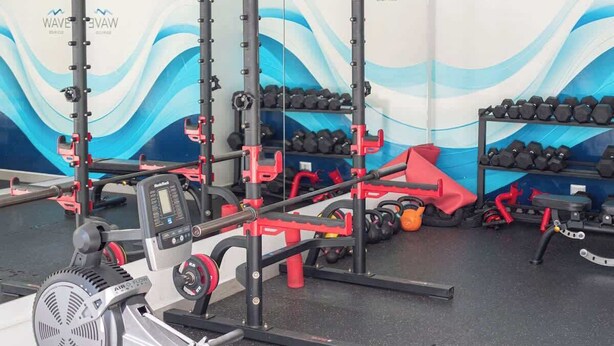 Uma academia com equipamentos de musculação, halteres e uma parede com a marca 'WAVE'.