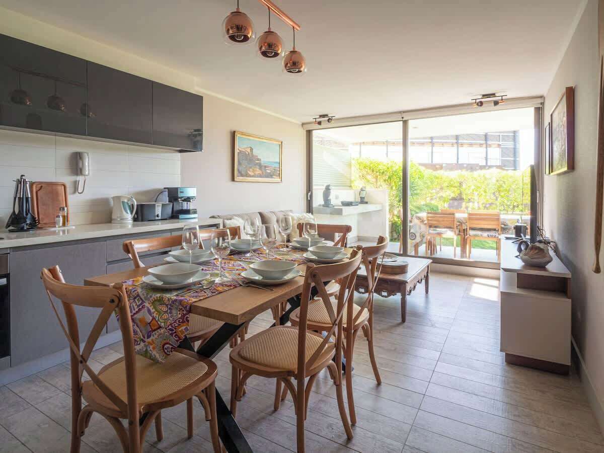 A modern kitchen with a dining area, large windows, and a view of the outdoors.