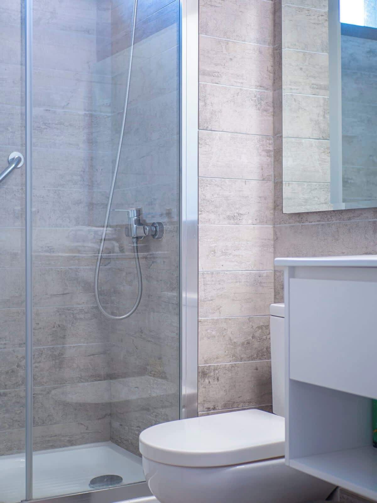 A modern bathroom with a glass shower enclosure, a white toilet, and a mirror above the sink.