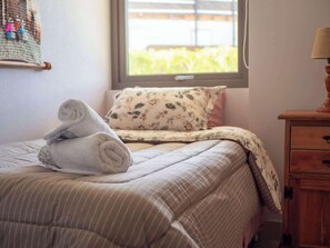 Ein ordentlich bezogenes Bett mit einer gestreiften Tagesdecke und einem Kopfkissen mit floralem Muster.