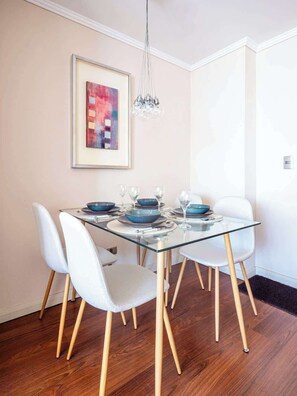 Uma sala de jantar com mesa de vidro, cadeiras brancas e um quadro abstrato emoldurado na parede.