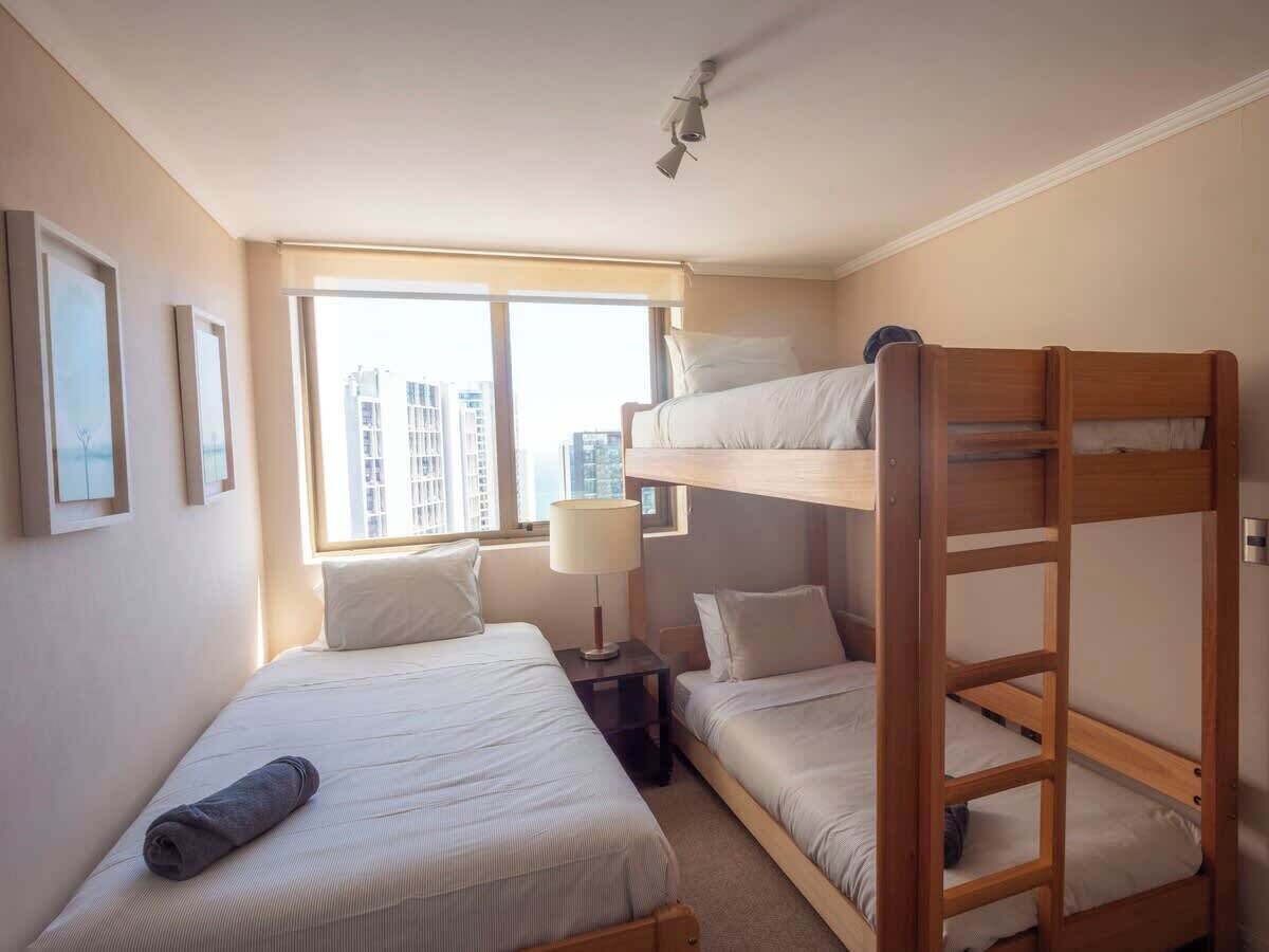 Ein Hotelzimmer mit Etagenbetten, einem Nachttisch mit Lampe und einem Fenster mit Blick auf die Stadt.