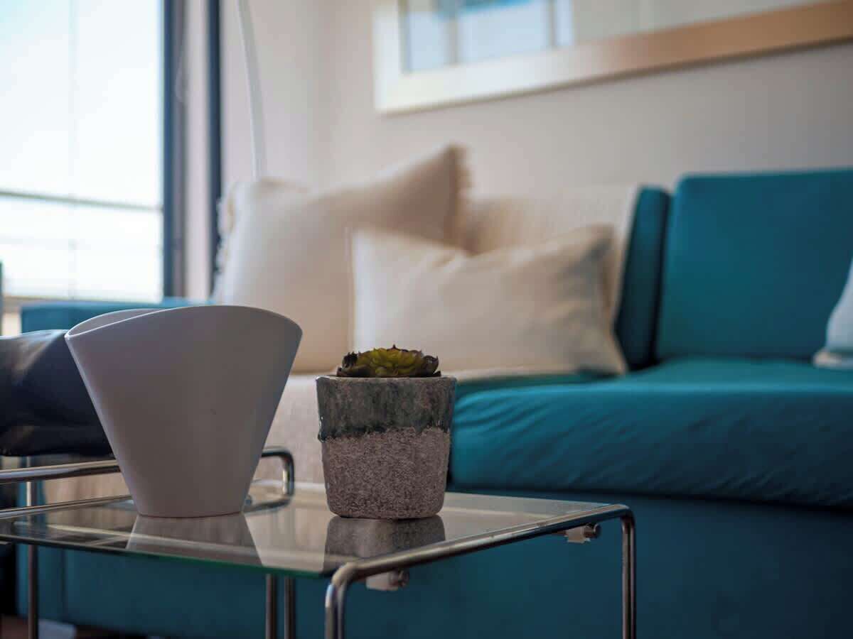 A modern living room with a teal sofa, a white vase, and a small potted plant on a glass table.