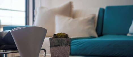 A modern living room with a teal sofa, a white vase, and a small potted plant on a glass table.