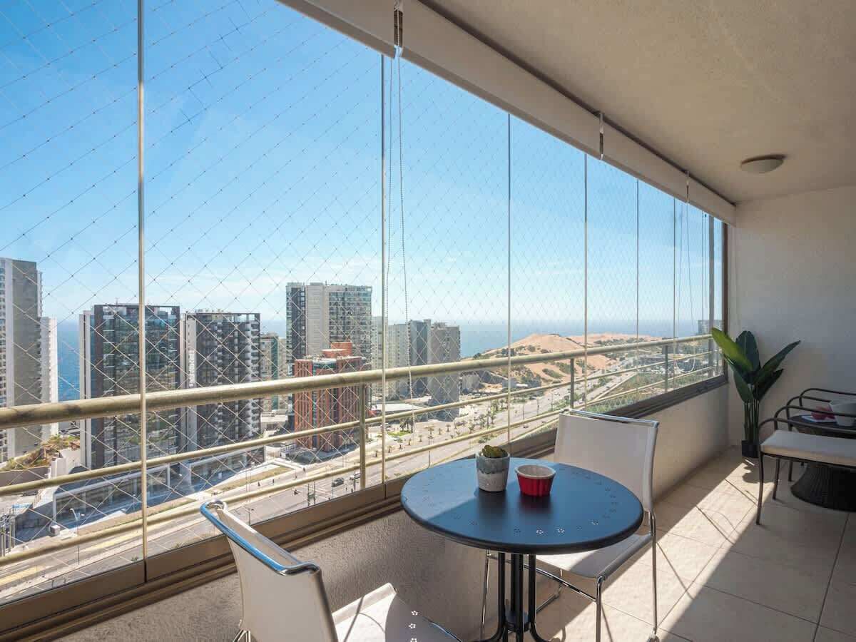 A balcony with a city view, a round table with chairs, and a potted plant.