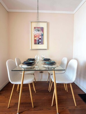 A dining area with a glass table, white chairs, and a framed abstract painting on the wall. - Costa Home - Departamento Zafiro 1 (Concón)