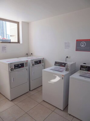 A laundry room with three stacked washing machines, a window, and a wall-mounted sign. - Costa Home - Departamento Zafiro 1 (Concón)