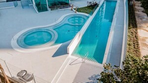 Uma área de piscina moderna com uma piscina retangular alongada, uma piscina circular menor e uma área de estar coberta.