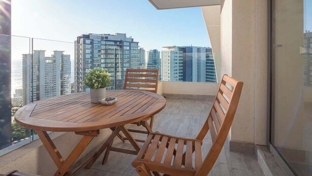 Varanda com mesa e cadeiras de madeira redonda, um vaso de planta e vista para edifícios altos.