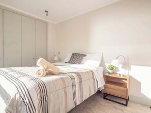 A bedroom with a bed, bedside table, lamp, and a plant. - Costa Home 4 PAX Edificio Wave WIFI (Concón)