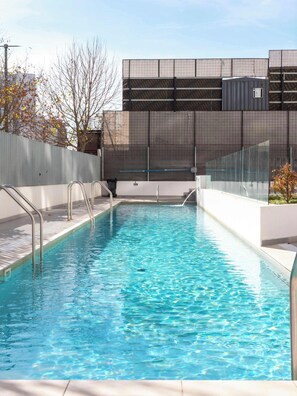 A rectangular swimming pool with metal handrails, surrounded by a low wall and a metal fence.