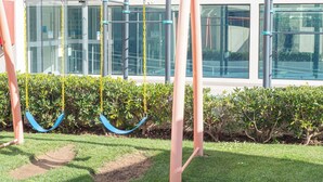 Um parquinho com balanços e uma estrutura de escalada em frente a um prédio moderno.
