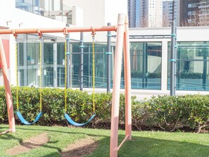 A playground with swings and a climbing structure in front of a modern building. - Costa Home 4 PAX Edificio Wave WIFI (Concón)