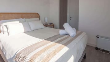 Un lit bien fait, recouvert d’une couverture à rayures, une table de chevet avec une lampe, et une porte sur le côté droit.