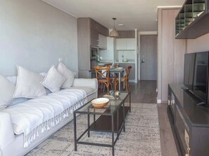 Un salon moderne avec un canapé, une table basse et un téléviseur. Il y a également un coin repas avec des chaises et une table.