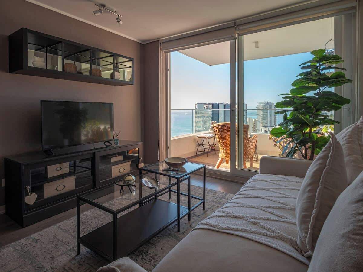 Una sala de estar con sofá, mesa de centro, televisor y un balcón con vistas a la ciudad.
