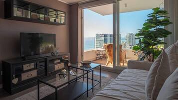 Una sala de estar con sofá, mesa de centro, televisor y un balcón con vistas a la ciudad.
