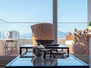 Un balcon avec une chaise en osier, une table sur laquelle se trouvent un saladier et un vase, et une vue sur le paysage urbain.