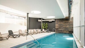 En inomhuspool med solstolar, en växt och en modern takdesign.