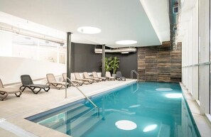 Ein Hallenbad mit Liegestühlen, einer Pflanze und einem modernen Deckenstil.
