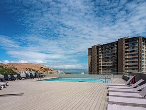 A rooftop pool area with lounge chairs and a view of a large building and hills. - Oceanview Apt w/ Pools, Paddel and many other amenities (Concón)