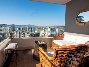 Ein Balkon mit Korbmöbeln, einem kleinen Tisch und Blick auf eine Stadtansicht.