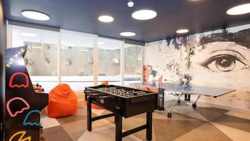 A room with a foosball table, a ping pong table, and a bean bag chair.