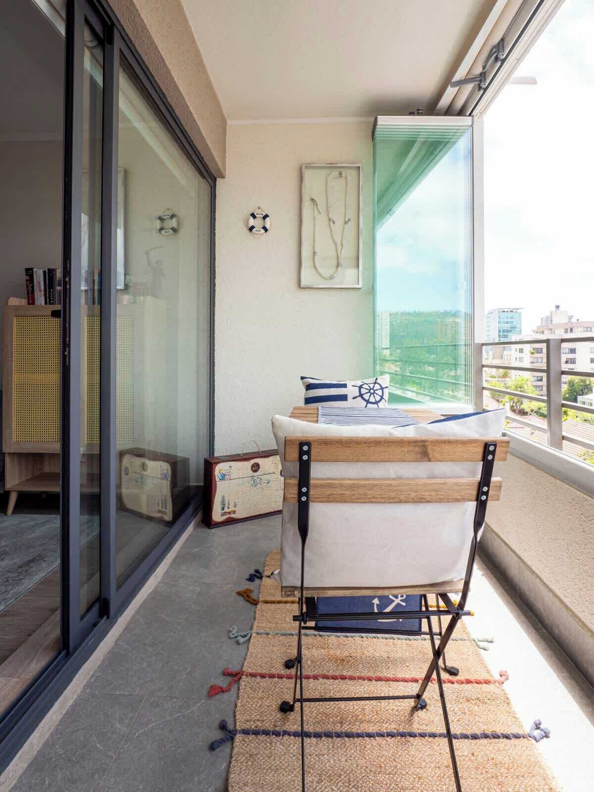 Ein Balkon mit Holzstuhl, einem kleinen Tisch, einem gerahmten Bild und Blick auf die Stadtlandschaft.