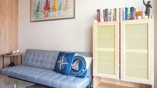 A modern living room with a grey sofa, a framed painting of sailboats, a bookshelf with books and a statue, and a coffee table. - Costa Home - Departamento La Marina (Viña del Mar)