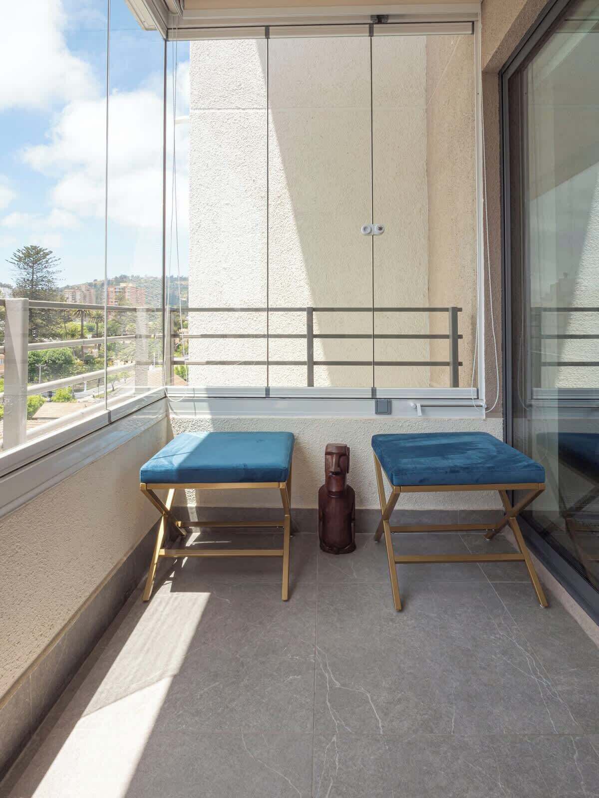A balcony with two blue cushioned benches, a small wooden statue, and a view of the cityscape. - Costa Home - Departamento La Marina (Viña del Mar)