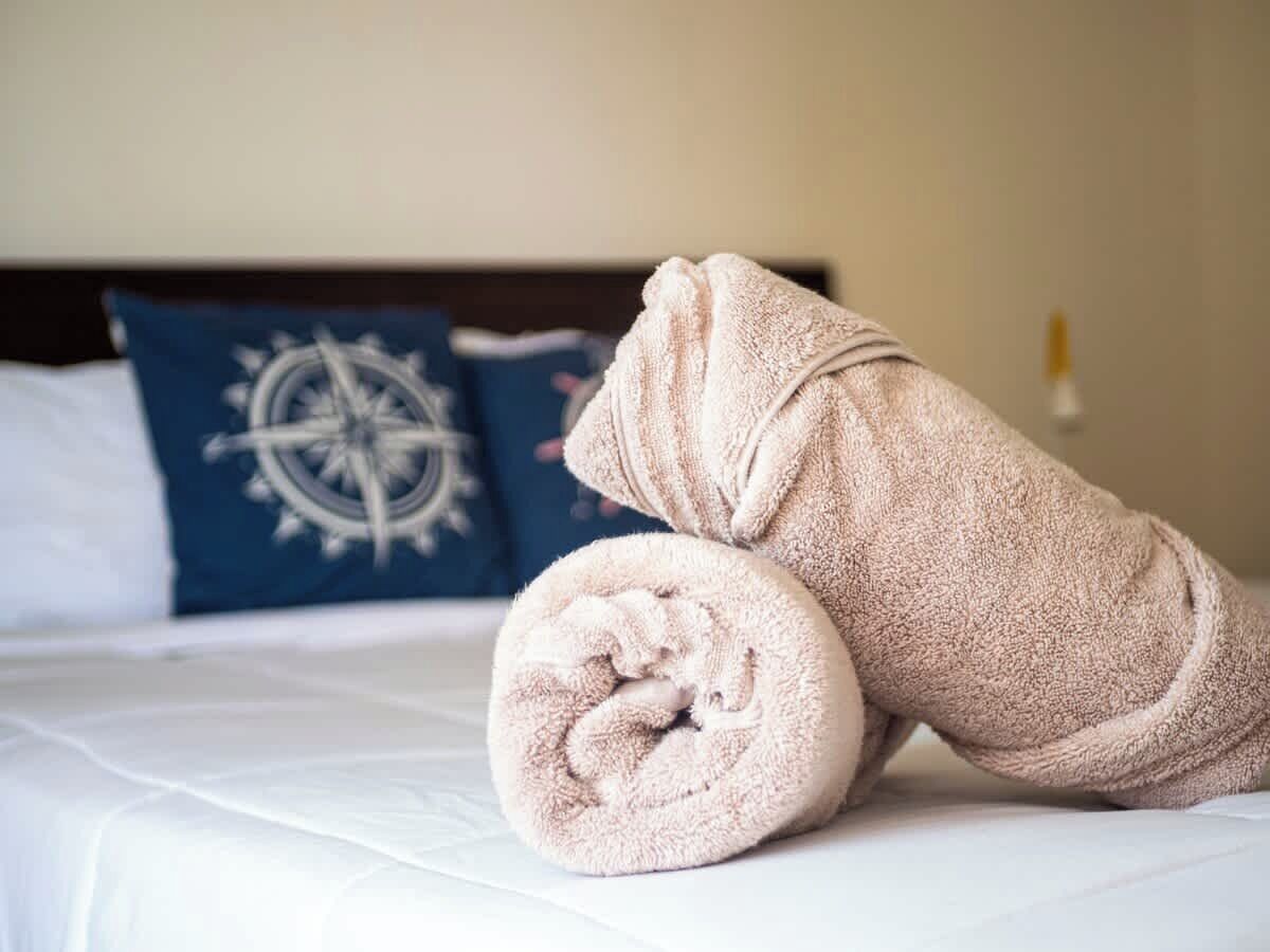 A neatly made bed with a rolled towel and a pillow with a compass design.