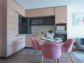 Une cuisine moderne avec des meubles en bois, un coin repas avec des chaises roses et une petite table dressée pour deux personnes.
