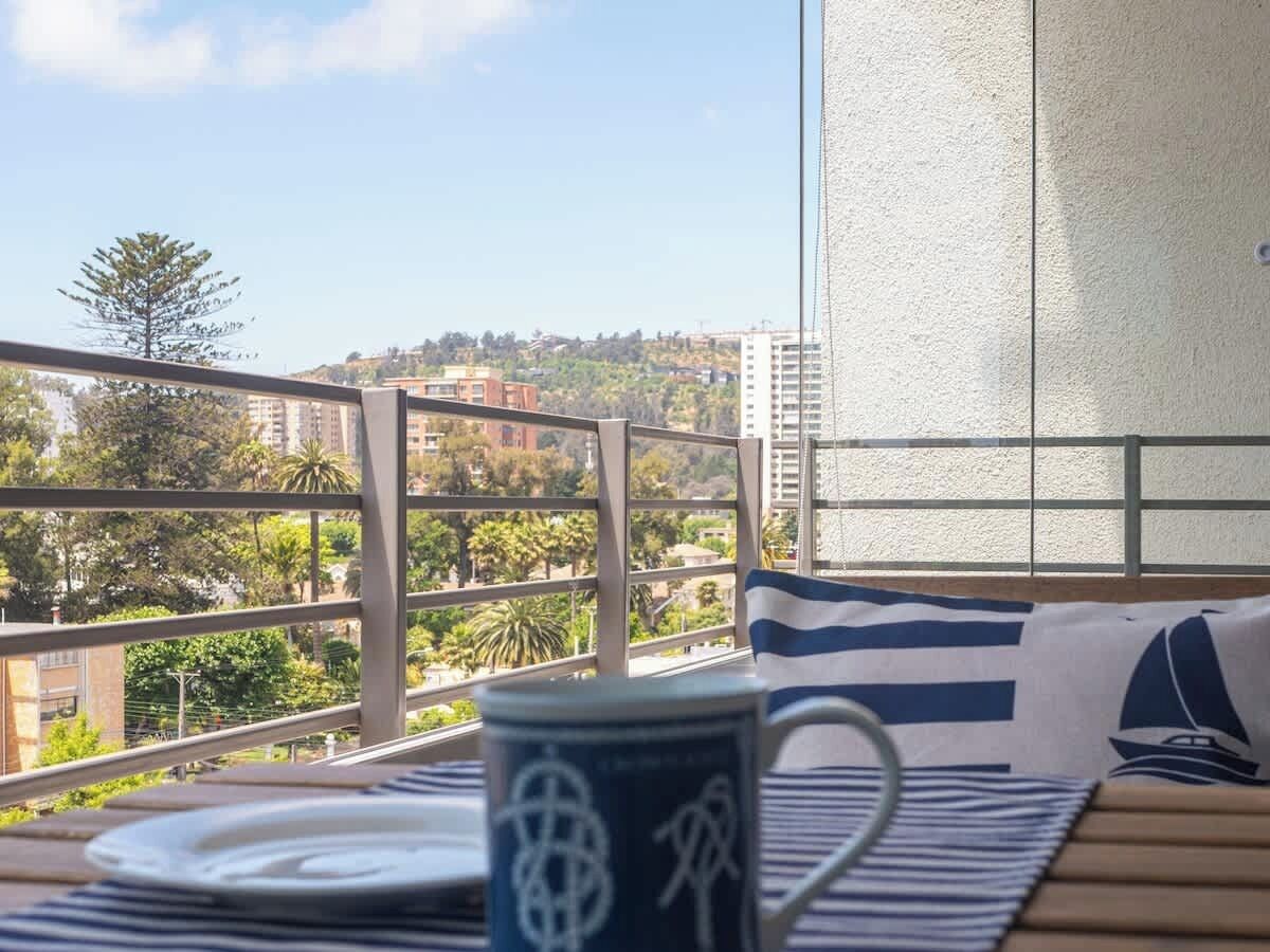 A balcony with a view of a cityscape, a table with a mug, and a striped pillow.