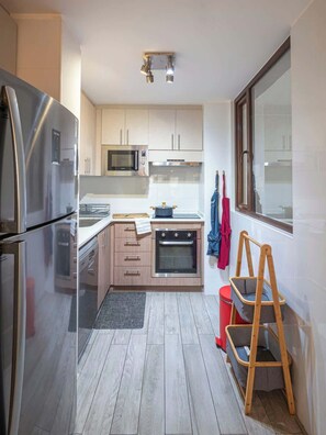 A compact kitchen with stainless steel appliances, wooden cabinets, a microwave, and a small oven. - Costa Home - Departamento Eluchans Plaza 1 (Viña del Mar)