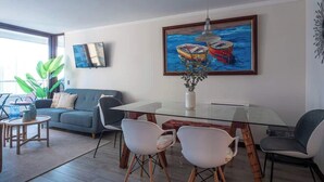 Una sala moderna con una mesa de comedor de vidrio, un sofá y un cuadro con barcos.