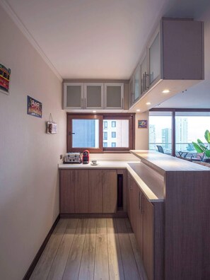 A modern kitchen with wooden cabinets, a built-in oven, and a window with a city view. - Costa Home - Departamento Eluchans Plaza 1 (Viña del Mar)