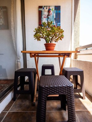 Ein Balkon mit einem Holztisch, drei Korbstühlen und einem Blumentopf.