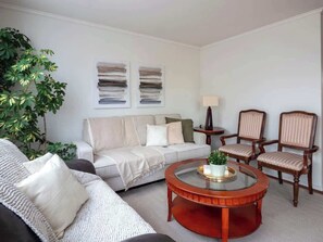 Ein Wohnzimmer mit einer Couch, zwei Sesseln, einem Couchtisch und einer Pflanze.
