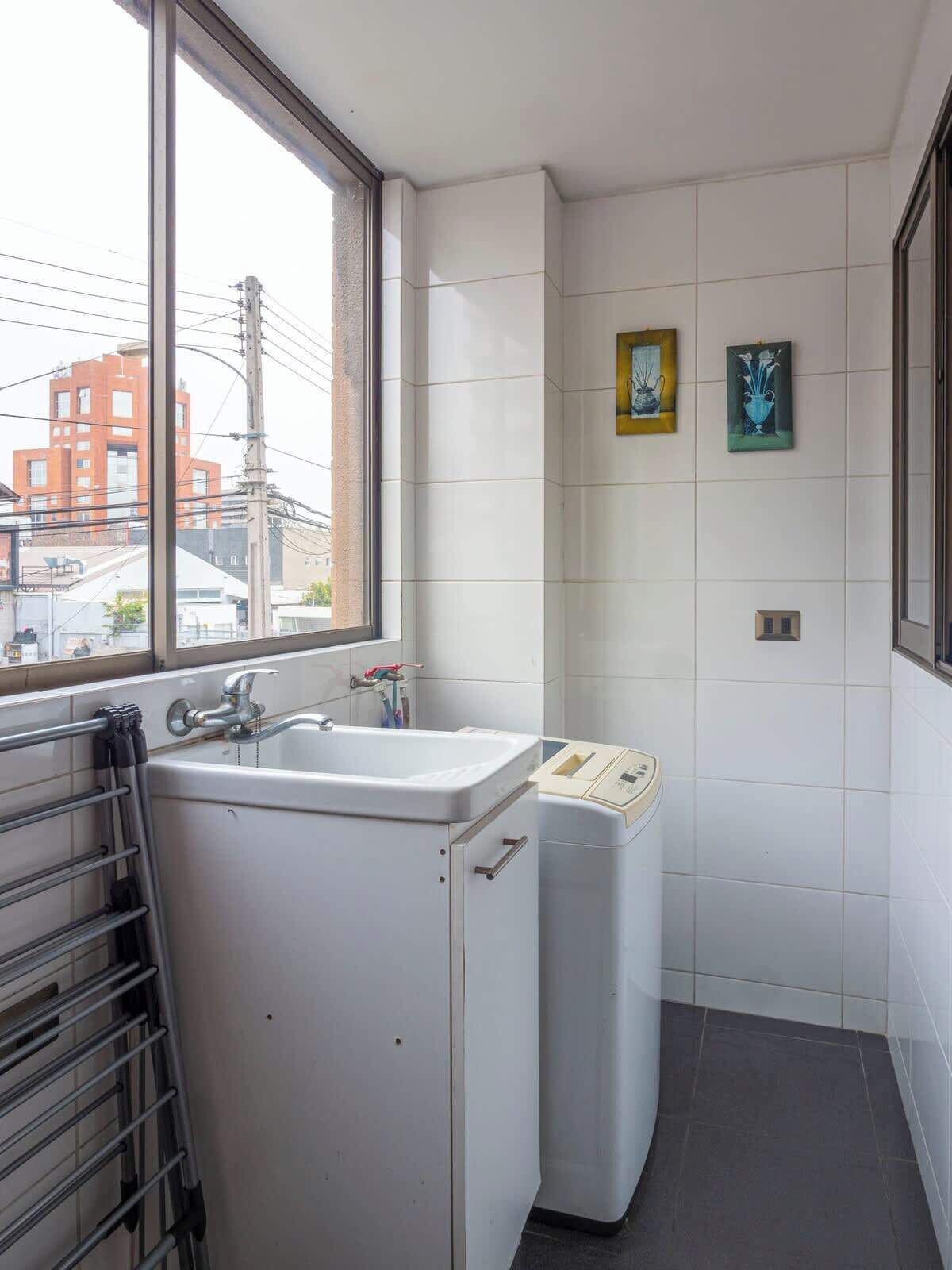 A small bathroom with a window, a sink, a towel rack, and two framed artworks on the wall.