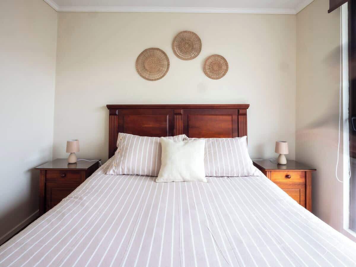 Un lit avec une tête de lit en bois, deux tables de chevet avec des lampes et trois éléments de décoration murale en fibres tressées.