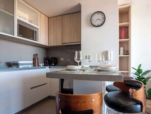 A modern kitchen with a dining area, wooden cabinets, a clock, and a plant. - Costa Home - Dpto EcoCostas Concón (Concón)