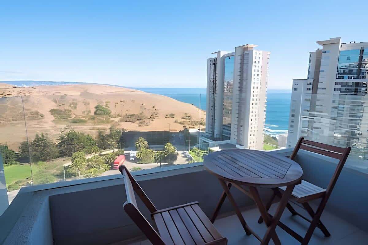 A balcony with a table and chairs, overlooking a desert landscape and a body of water.
