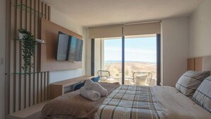 Ein Schlafzimmer mit einem Bett, einem Fernseher, einer Pflanze, einem Sessel und Blick auf die Wüste.