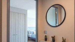 A hallway with a wooden floor, a wardrobe, a mirror, and a bed in the adjacent room. - Apartamento 1 Habitación Quinta Vergara (Viña del Mar)