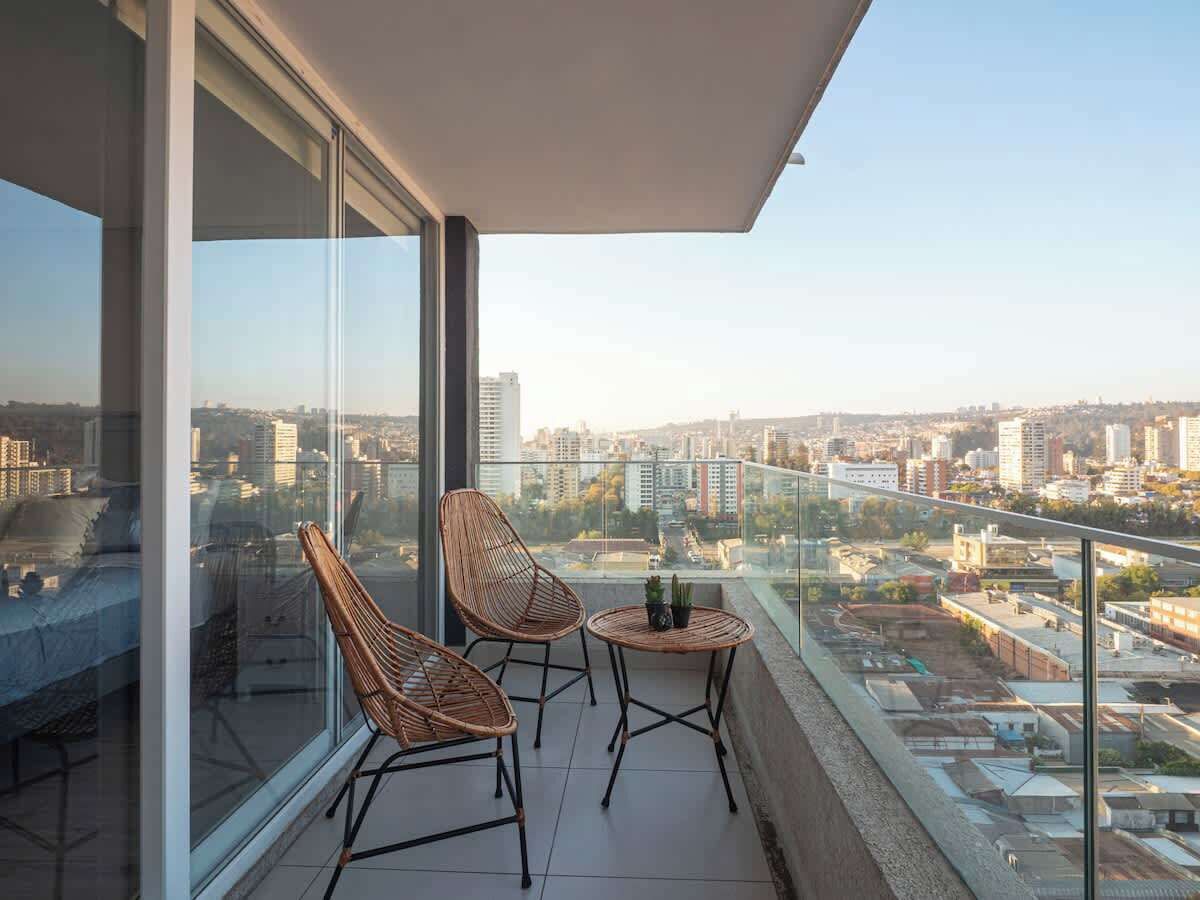 A balcony with two wicker chairs and a small table, overlooking a cityscape.