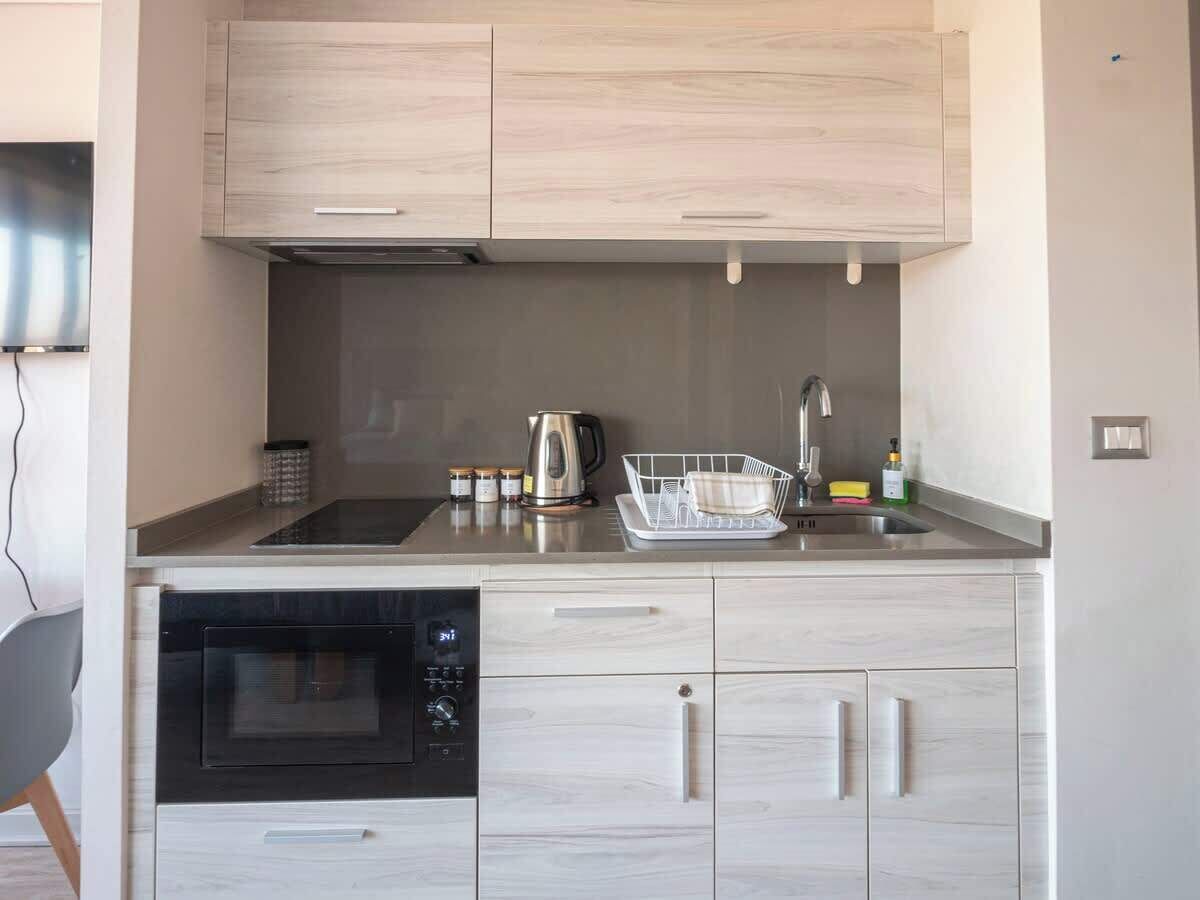 A modern kitchen with a built-in oven, stainless steel countertops, and light wood cabinetry.