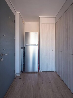Ein schmaler Flur mit einem Edelstahl-Kühlschrank, einer Tür mit Griff und einem Holzboden.