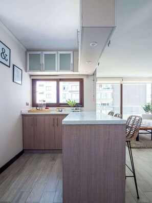 A modern kitchen with wooden cabinets, a central island, and a dining area with a chair.