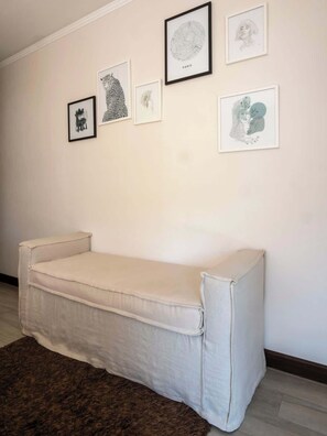 Una habitación con un sofá blanco, un tapete marrón y cinco obras de arte enmarcadas en la pared.
